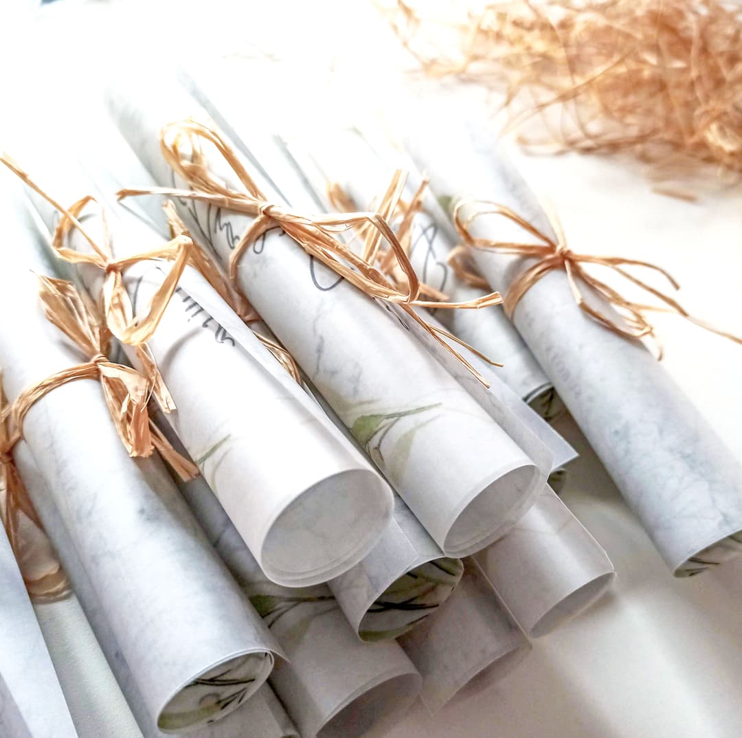 Svaka je pozivnica pažljivo zarolana i vezana rafijom - jednostavno, toplo i prirodno, baš onako kako su Ana i Ivica zamislili. Tisak na prozračnom paus papiru donosi laganu, gotovo sanjivu notu, dok ručna izrada svakog primjerka s posebnom pažnjom i ljubavlju potvrđuje da upravo sitnice čine razliku.